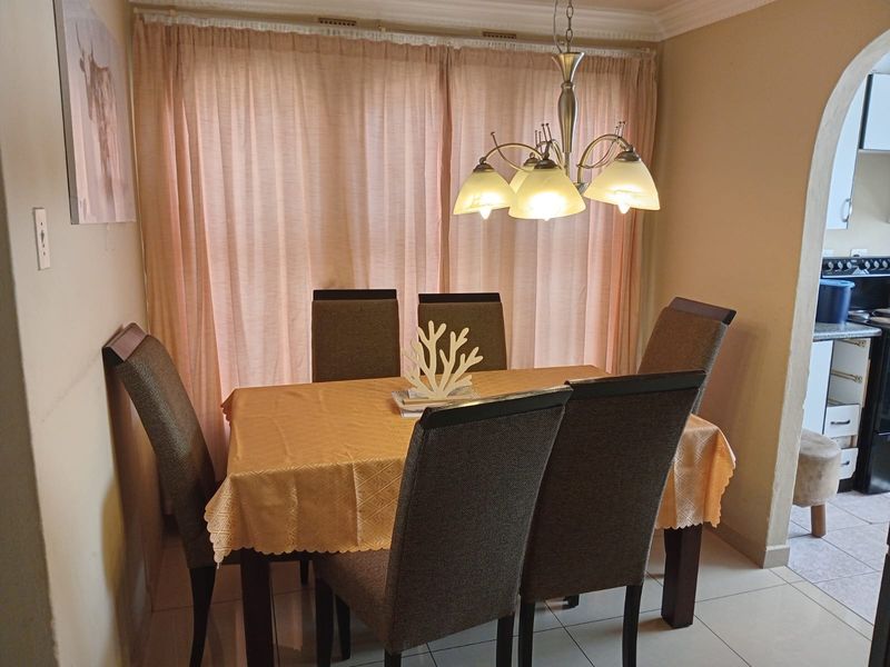 A dining room featuring tiled flooring, a decorative pendant light fixture, and an arched entryway leading to the kitchen area.