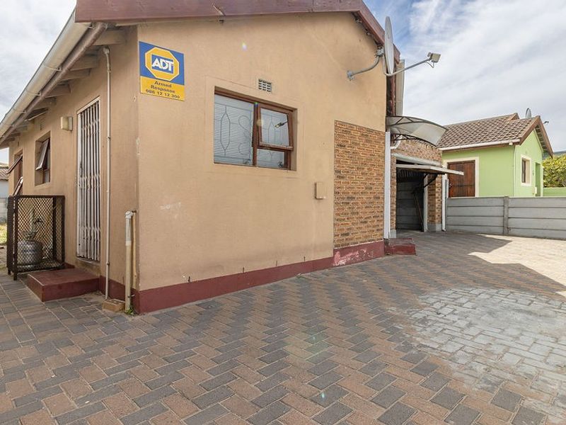 Rear exterior view of the property featuring a paved driveway, brick accents, and secure perimeter walling.