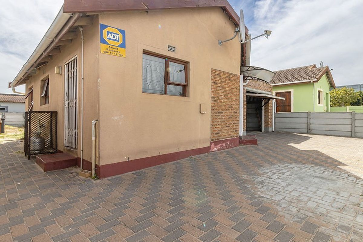 Rear exterior view of the property featuring a paved driveway, brick accents, and secure perimeter walling.
