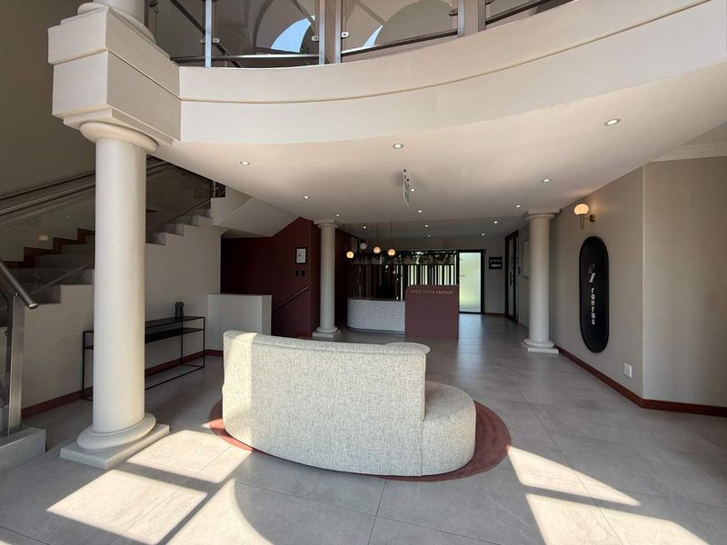 A bright and modern office building entrance lobby featuring a reception desk, tiled floors, and a grand staircase with glass balustrades.