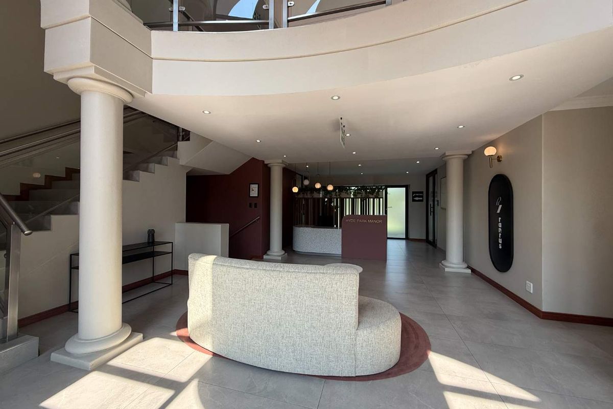 A bright and modern office building entrance lobby featuring a reception desk, tiled floors, and a grand staircase with glass balustrades.
