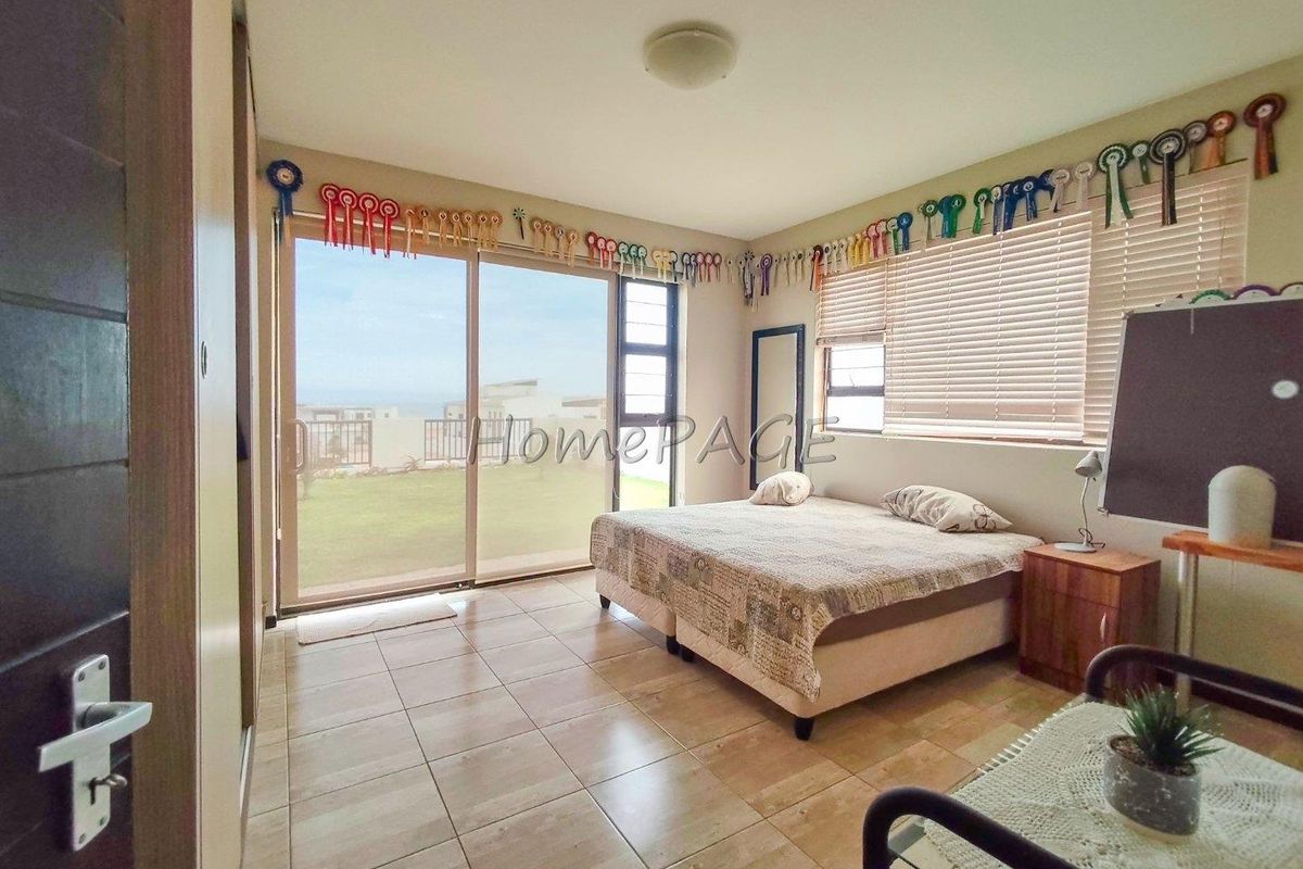 Spacious bedroom featuring large sliding glass doors that open to a garden view, tiled flooring, and built-in cupboards.