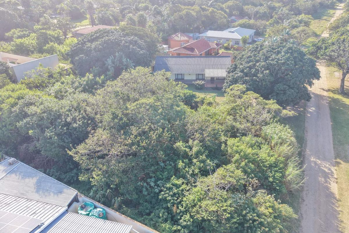 Aerial view of a residential property featuring dense vegetation, metal roofing, solar panels, and water storage tanks in a suburban setting.