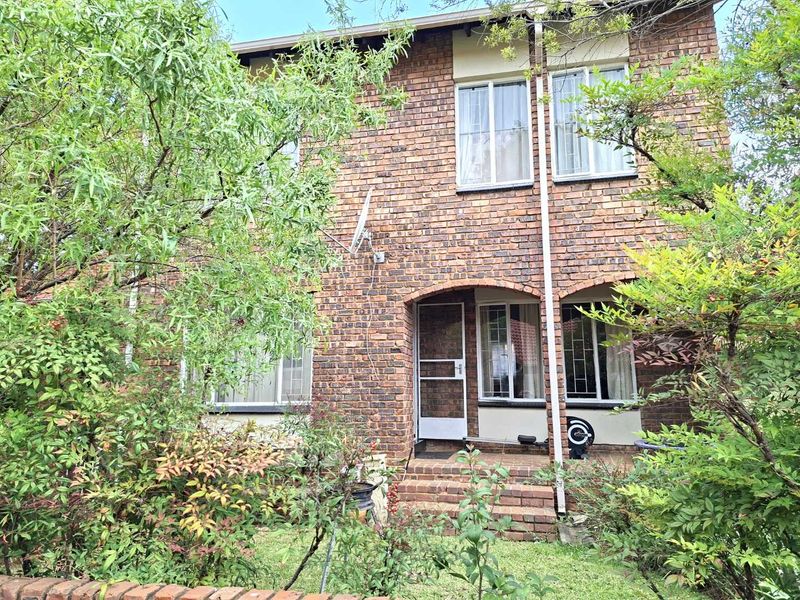 Rear view of a two-story face brick townhouse featuring a small patio area and established garden surroundings.