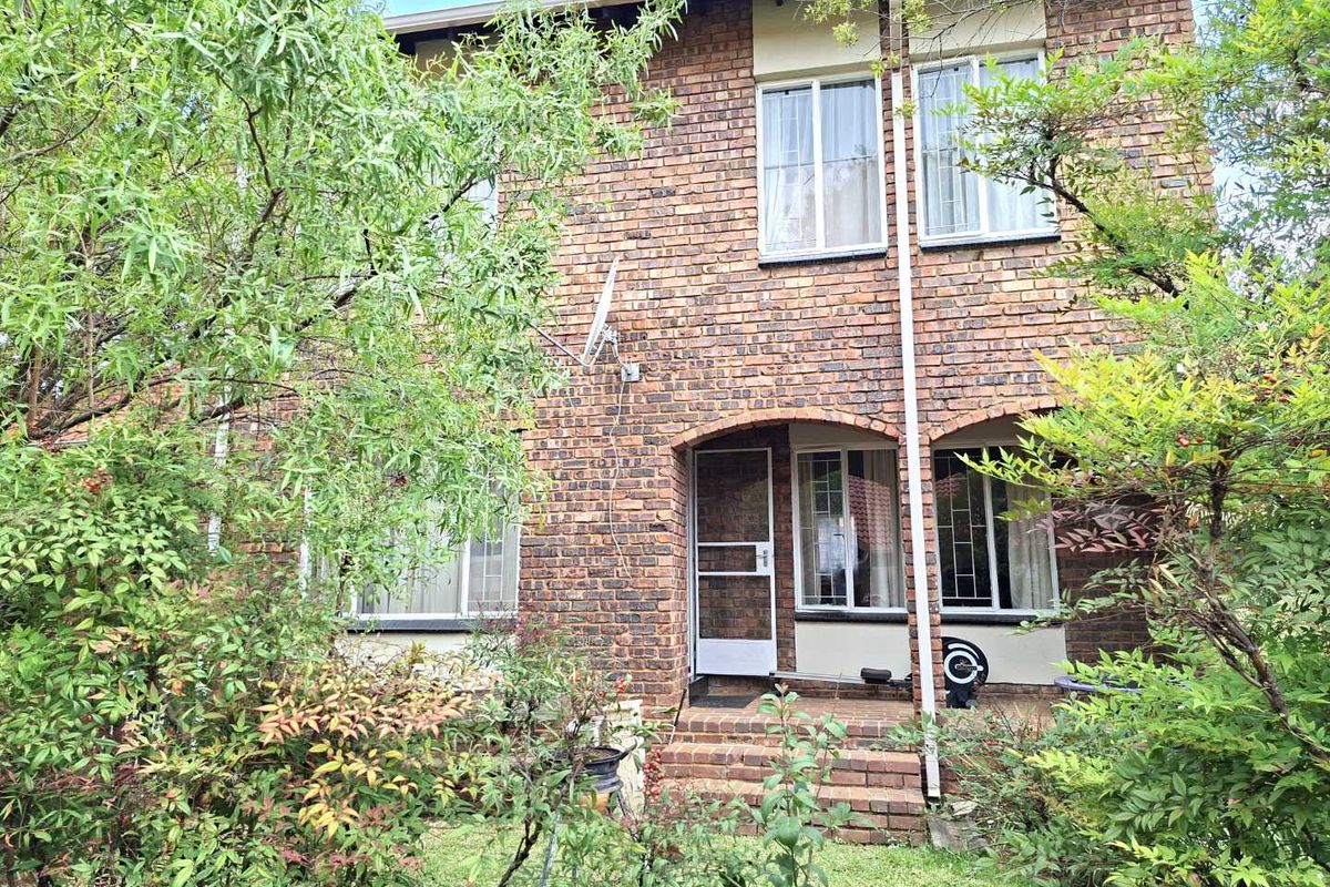 Rear view of a two-story face brick townhouse featuring a small patio area and established garden surroundings.