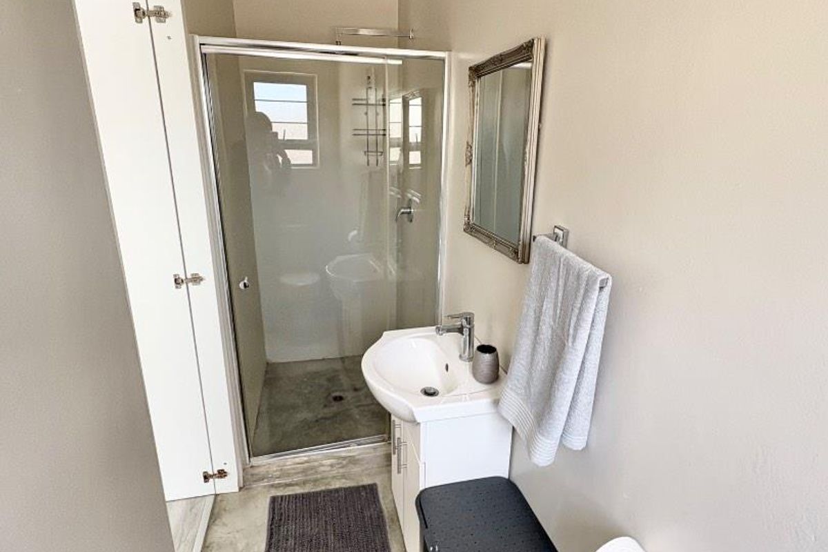 A compact bathroom featuring a glass-enclosed shower, a modern pedestal vanity with basin, and neutral wall finishes.