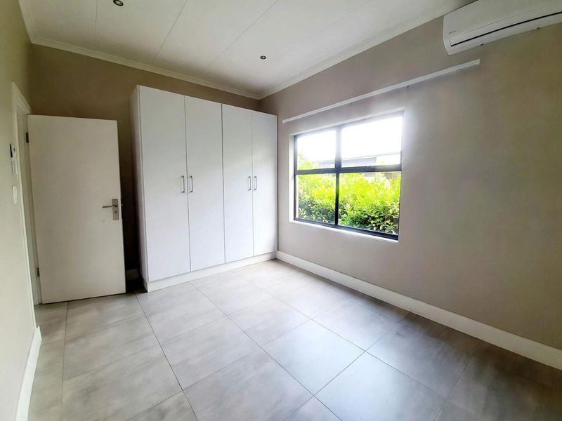 A bright, empty bedroom featuring modern tiled flooring, built-in cupboards, and a wall-mounted air conditioning unit.