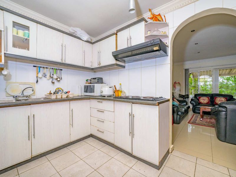 Functional kitchen featuring white cabinetry, built-in hob, extractor fan, and tiled flooring, with an open archway leading into the adjacent living area.