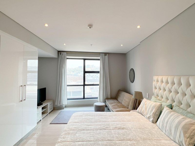 A well-maintained bedroom featuring a large built-in wardrobe, recessed ceiling lighting, and a large window providing natural light and city views.