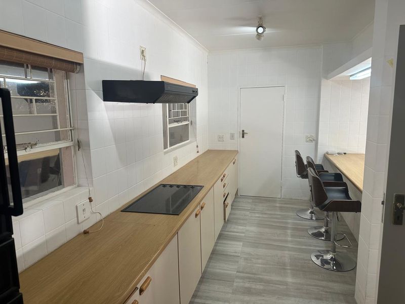 A functional kitchen featuring light-toned cabinetry, laminate countertops, an integrated electric hob with extractor fan, and tiled wall finishes.