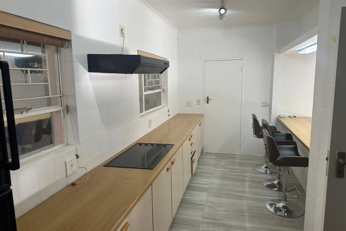 A functional kitchen featuring light-toned cabinetry, laminate countertops, an integrated electric hob with extractor fan, and tiled wall finishes.