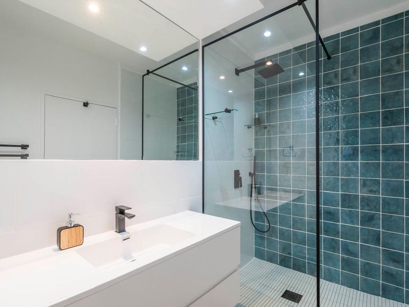 Modern bathroom featuring a walk-in shower with blue feature tiling, a sleek wall-mounted vanity with integrated basin, and a large mirror.