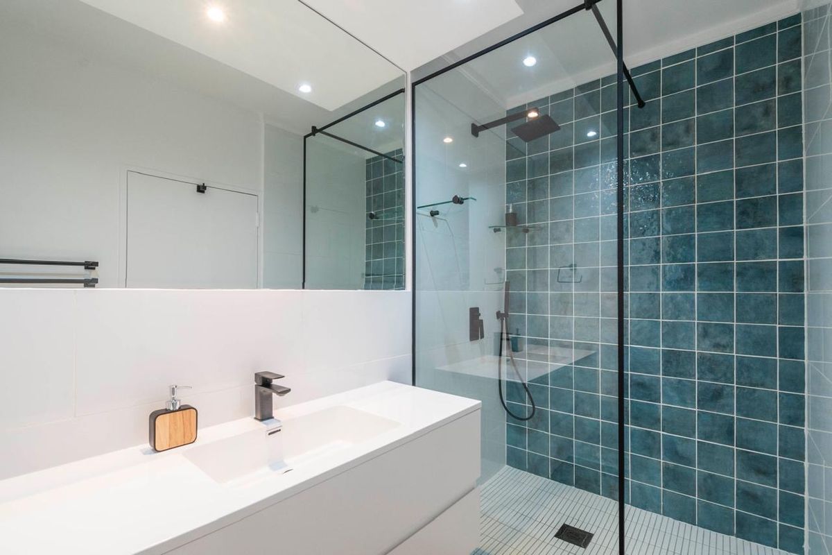 Modern bathroom featuring a walk-in shower with blue feature tiling, a sleek wall-mounted vanity with integrated basin, and a large mirror.