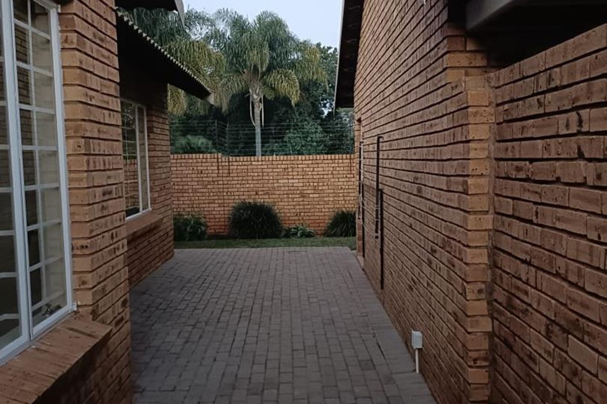 A paved side walkway between two brick townhouse structures, leading to a rear garden area enclosed by a brick boundary wall.