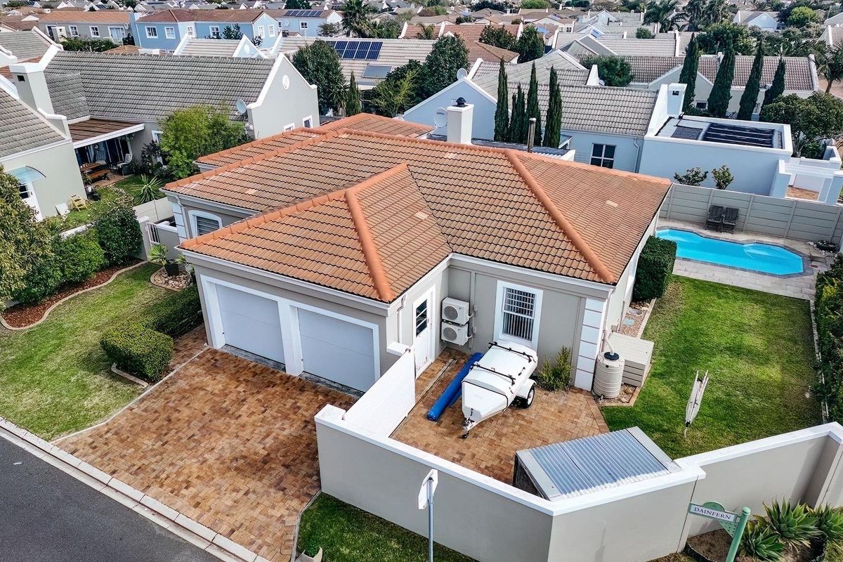 Aerial view of a residential property featuring a tiled roof, double garage, paved driveway, private swimming pool, and landscaped garden area.