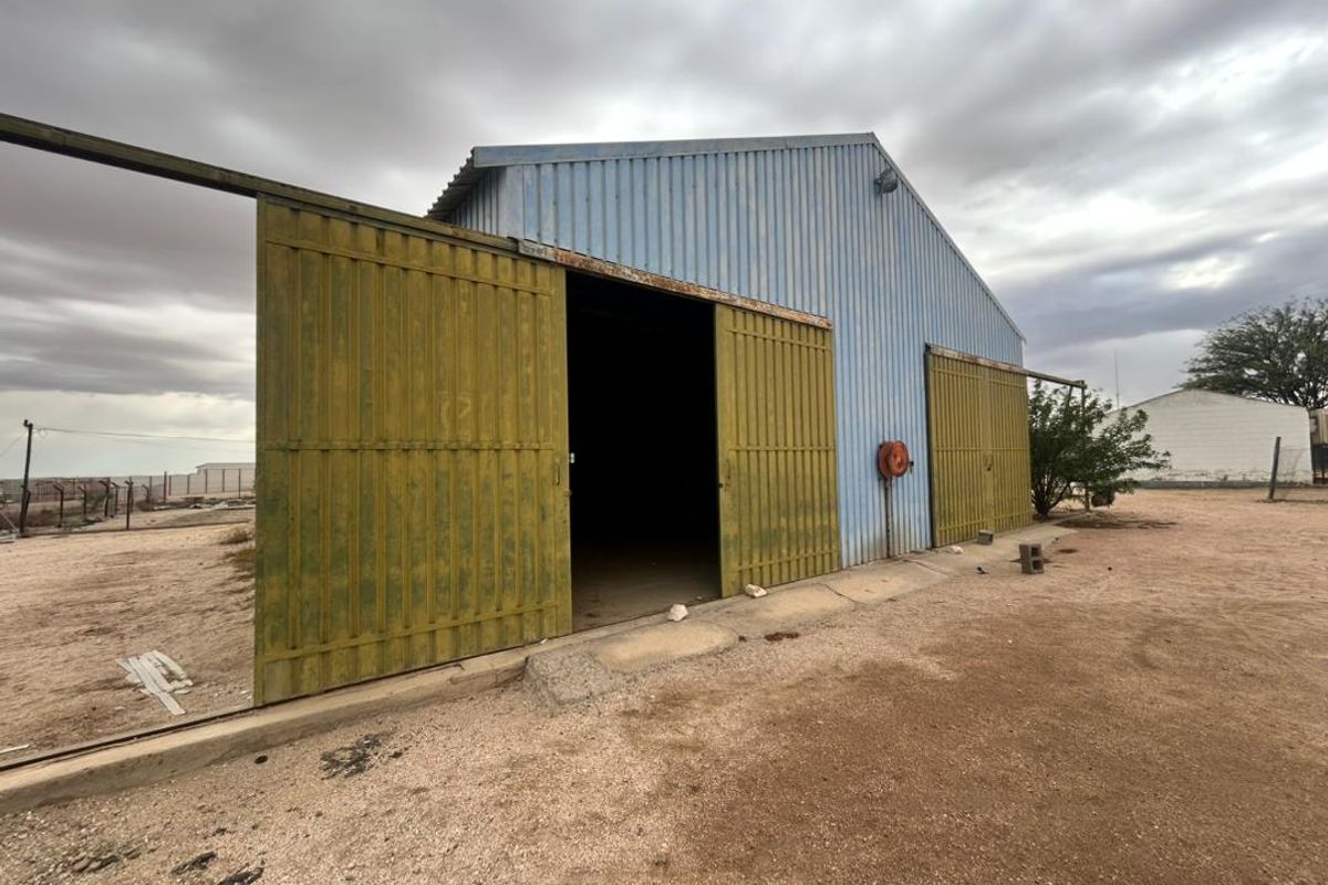 Exterior view of an industrial warehouse featuring large sliding metal doors, corrugated metal cladding, and a fire hose reel mounted on the side.