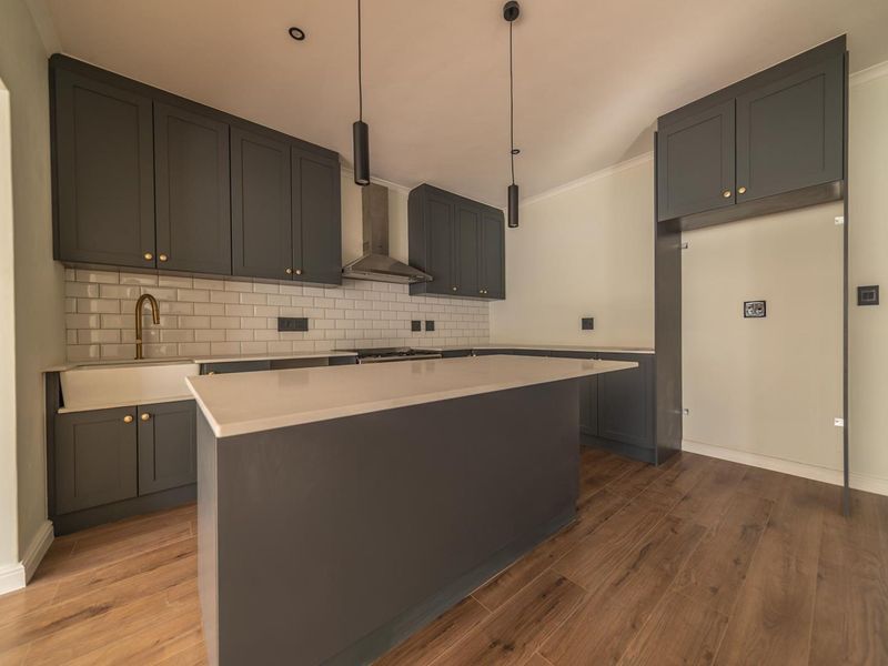 Modern kitchen featuring dark grey shaker-style cabinetry, white quartz countertops, subway tile backsplash, a central island, and high-quality brass fixtures.