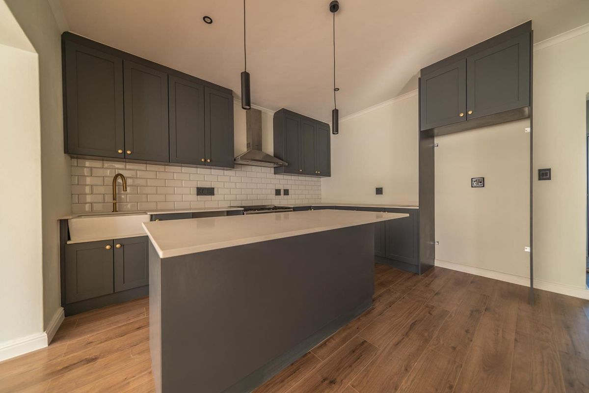 Modern kitchen featuring dark grey shaker-style cabinetry, white quartz countertops, subway tile backsplash, a central island, and high-quality brass fixtures.