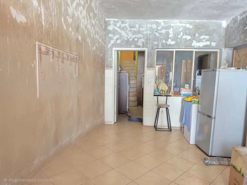 A kitchen area featuring tiled flooring and a pass-through window, currently requiring significant wall finishing and renovation to complete the space.