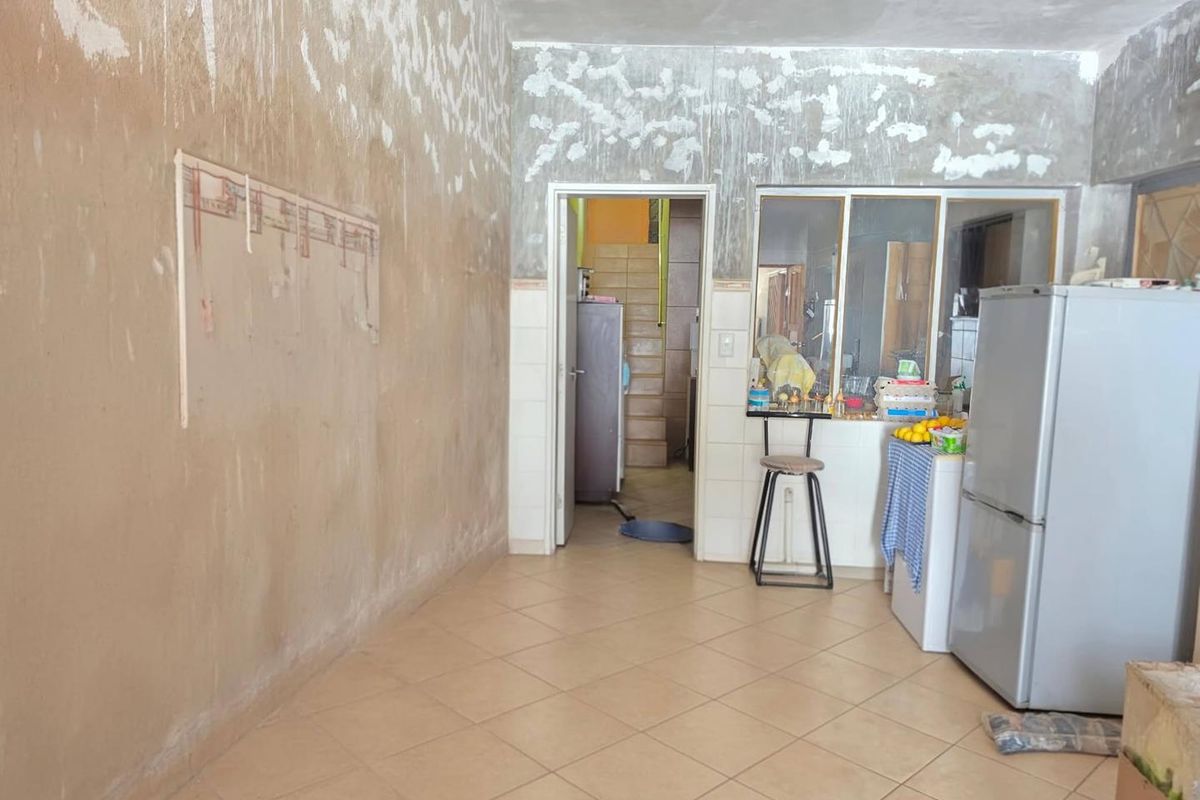 A kitchen area featuring tiled flooring and a pass-through window, currently requiring significant wall finishing and renovation to complete the space.