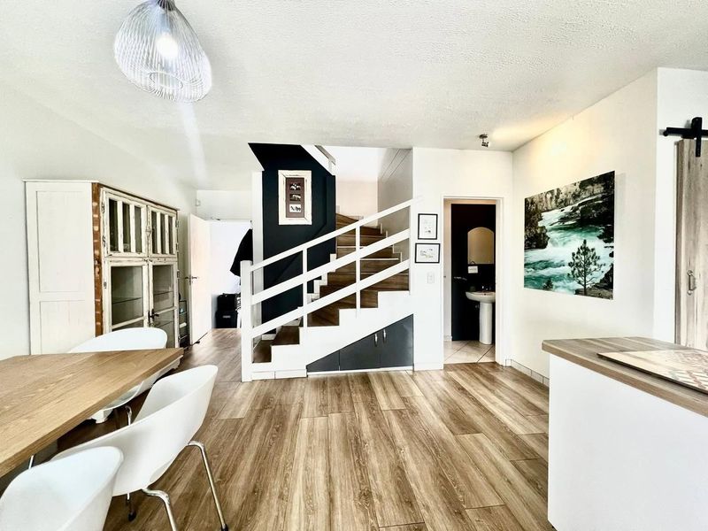 Open plan living area featuring modern laminate flooring, a central staircase with integrated storage, and access to a guest bathroom.