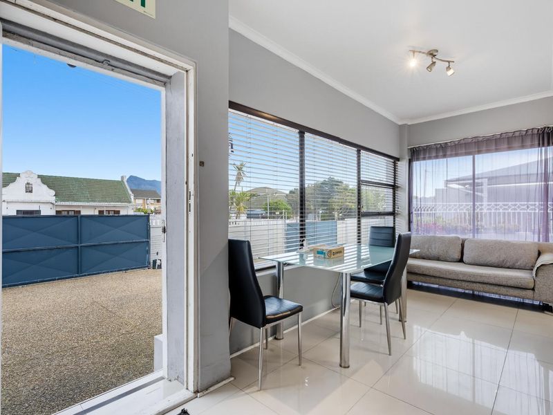 Bright living area featuring large windows with venetian blinds, tiled flooring, and direct access to the exterior through a sliding door.