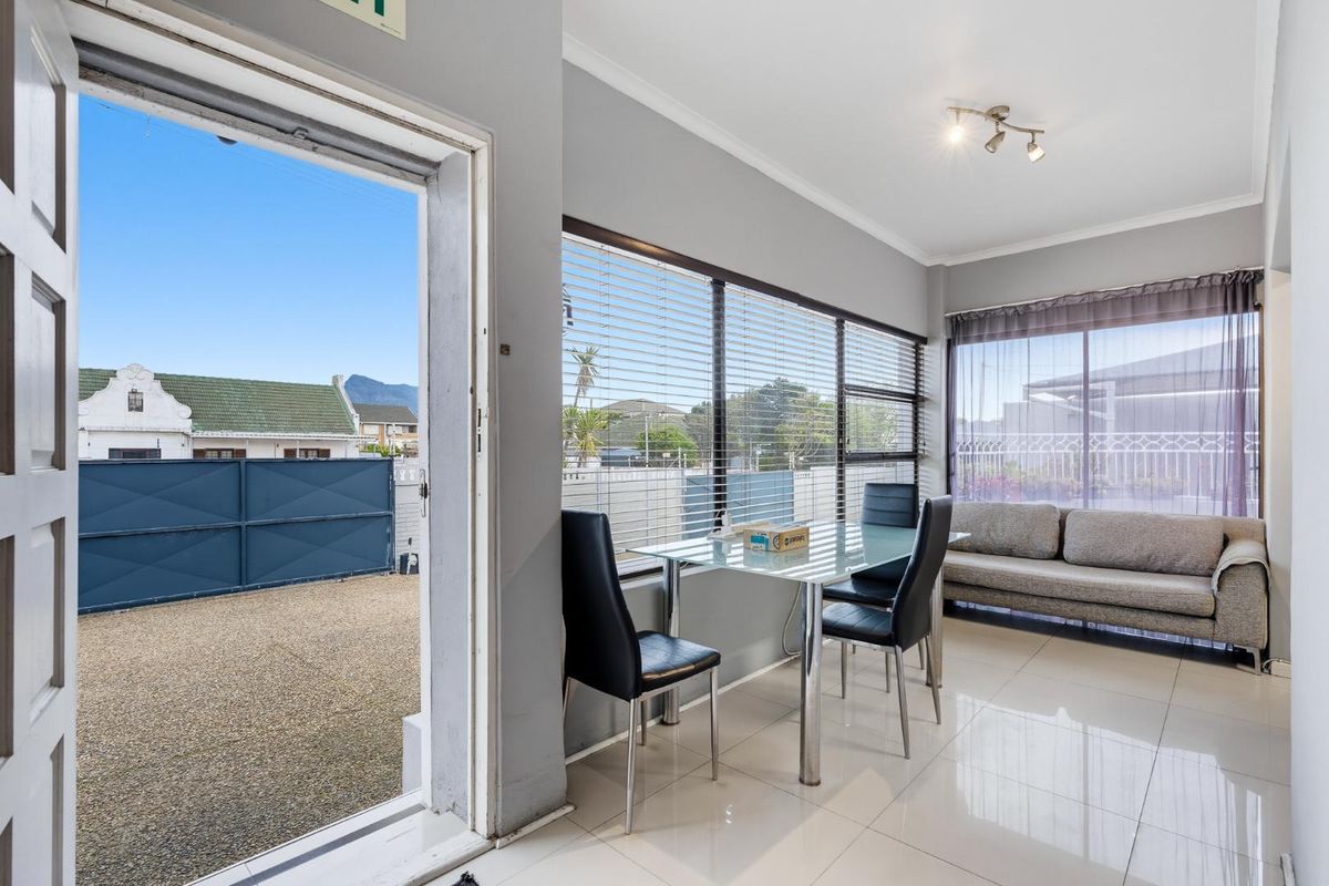 Bright living area featuring large windows with venetian blinds, tiled flooring, and direct access to the exterior through a sliding door.