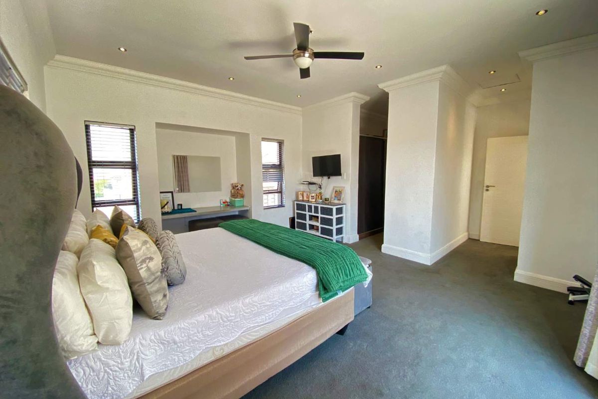 Spacious bedroom featuring a built-in vanity, integrated cupboard space, ceiling fan, and recessed lighting with neutral finishes.