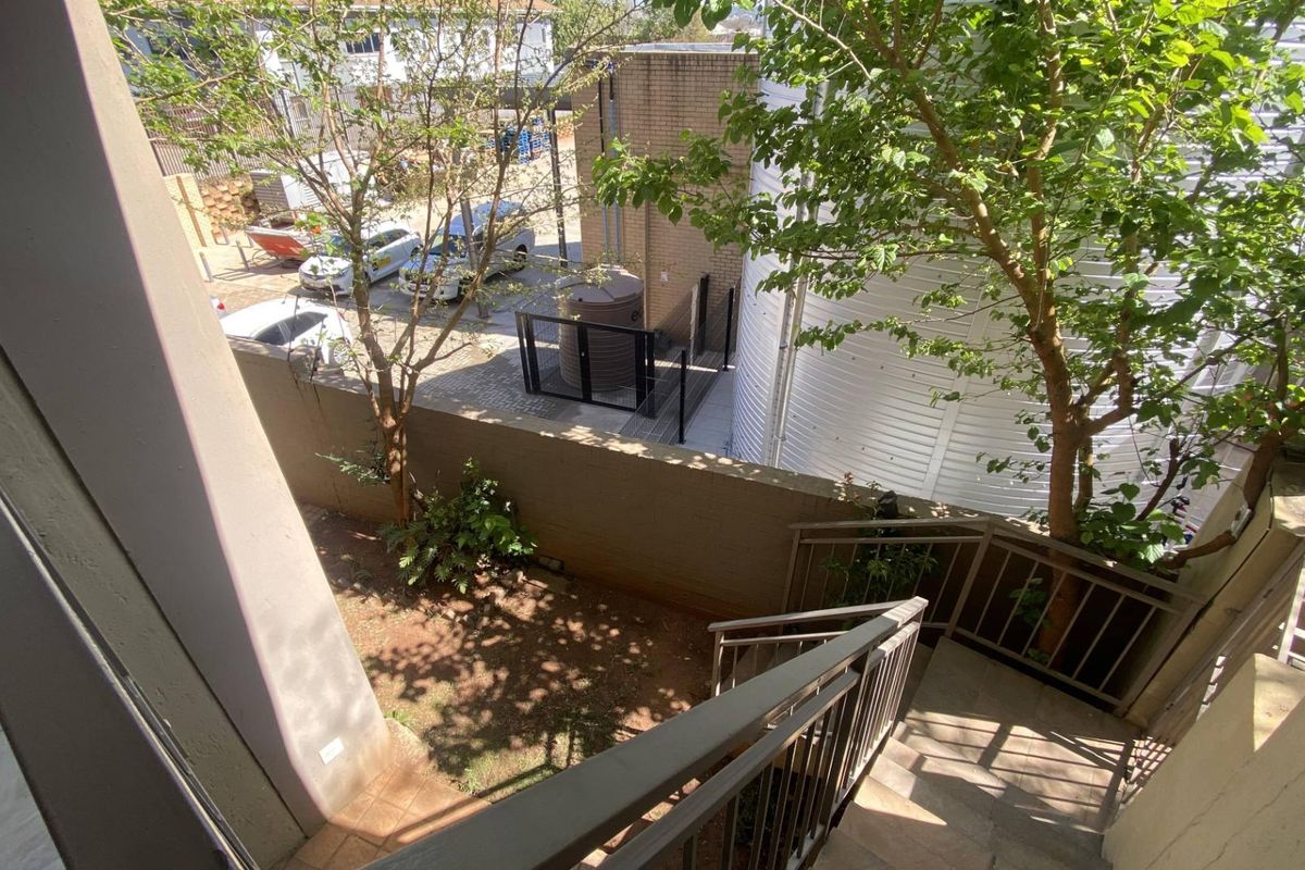 An elevated view of a rear exterior area featuring a metal staircase leading down to a small garden space and paved driveway.