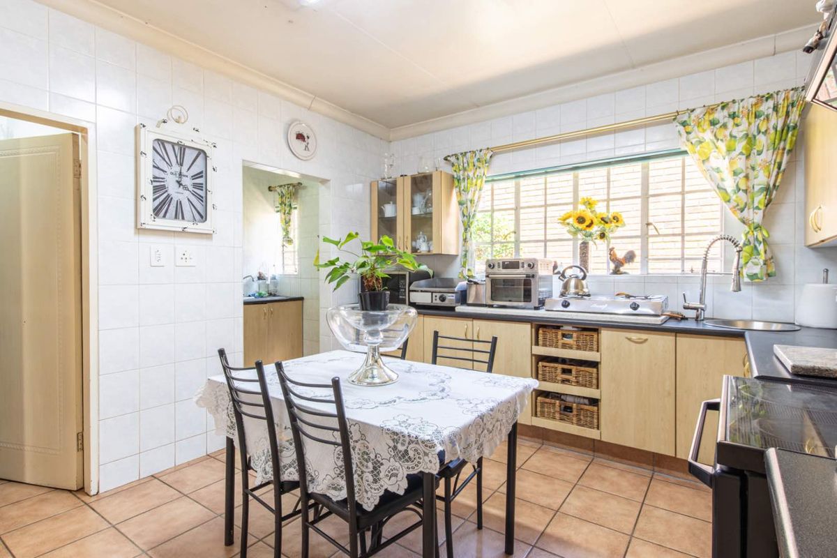 A functional kitchen featuring tiled walls, laminate cabinetry, and a tiled floor, with an adjacent scullery area visible through the doorway.