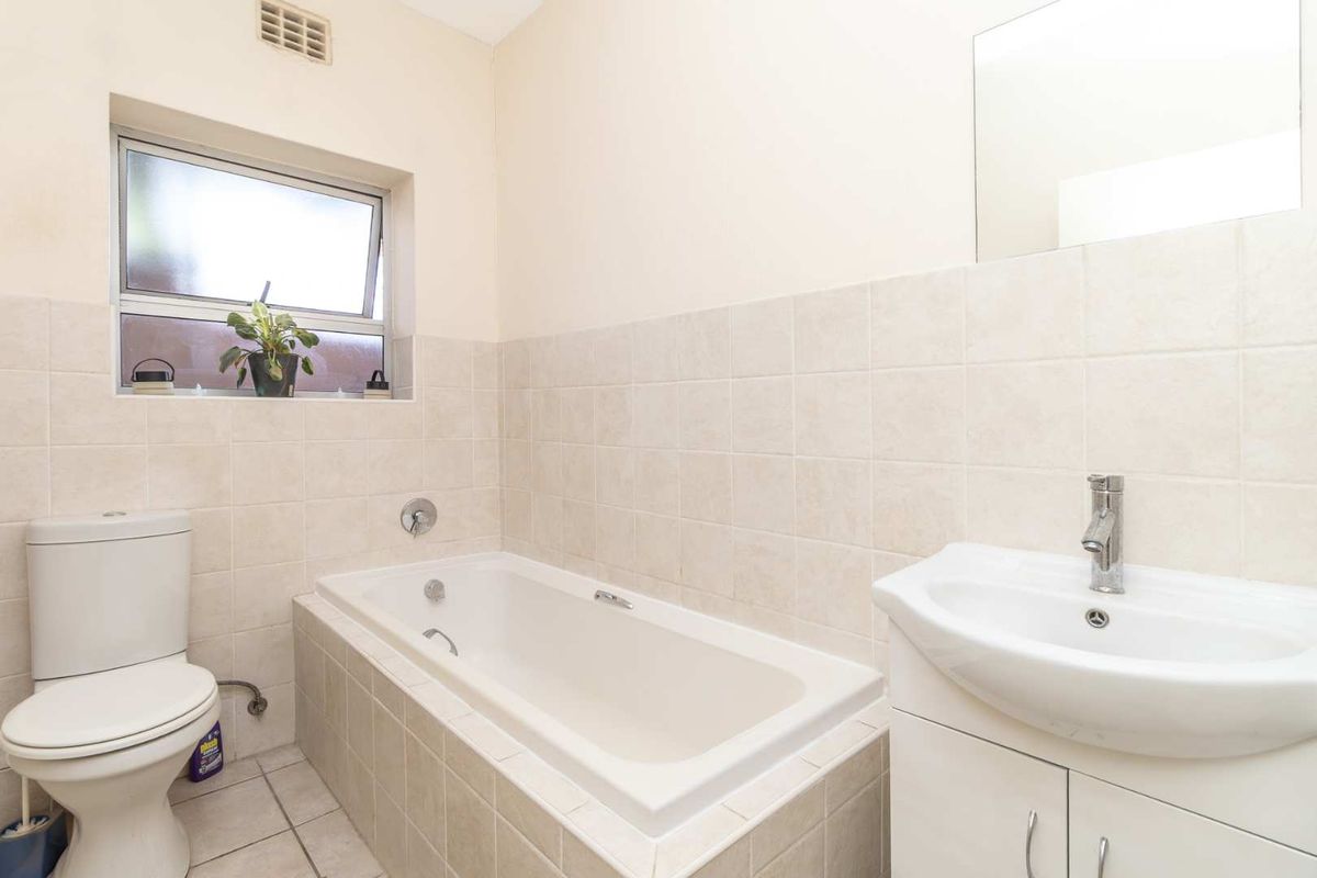 A functional bathroom featuring a built-in bathtub, a pedestal vanity with a basin, and a standard toilet, finished with neutral wall tiles.