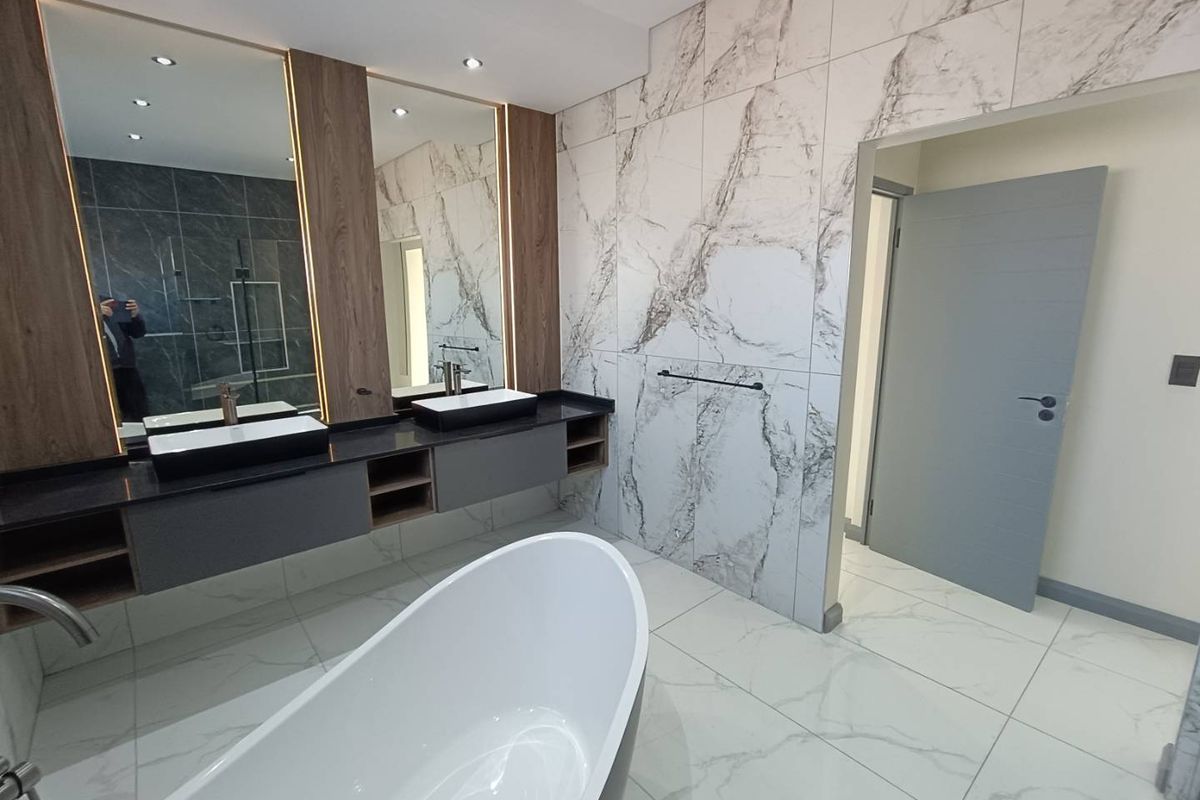 Modern luxury bathroom featuring a freestanding bathtub, double vanity with vessel sinks, and elegant marble-look wall tiling with integrated LED lighting.