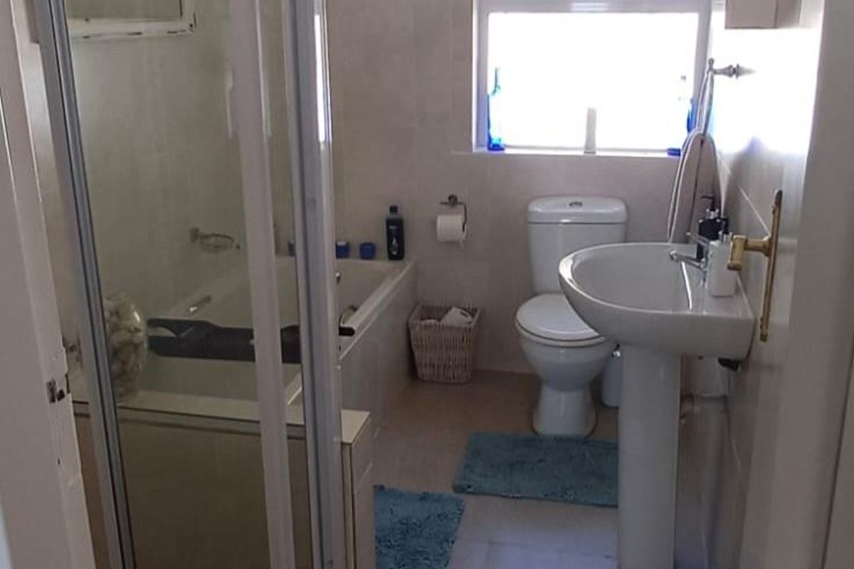A functional bathroom featuring a pedestal basin, a toilet, and a combined shower and bathtub unit with a glass enclosure.