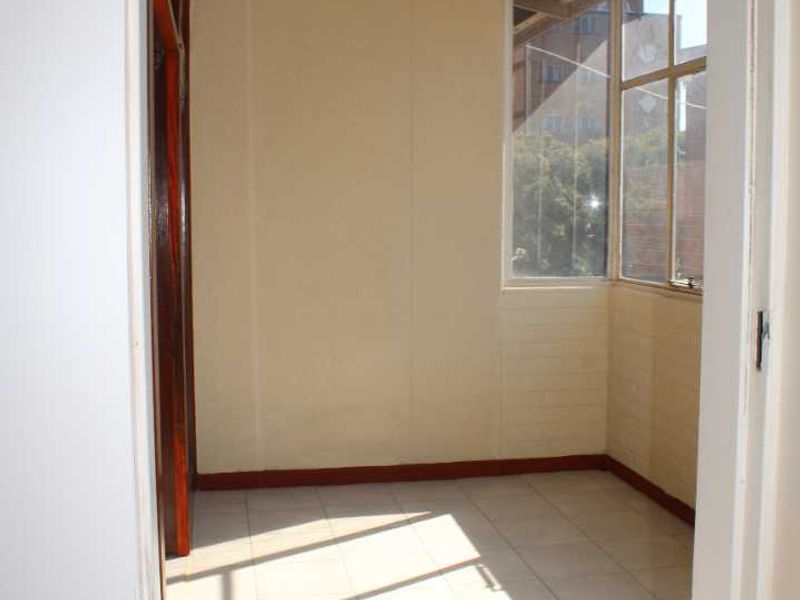 A bright, empty enclosed balcony or sunroom featuring tiled flooring and large windows, offering a versatile space for a home office or relaxation area.