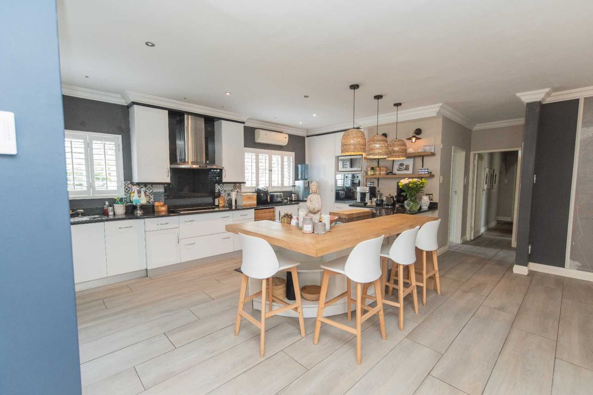 Modern open-plan kitchen featuring white cabinetry, a central island with a wooden countertop, stainless steel extractor fan, and tiled flooring.