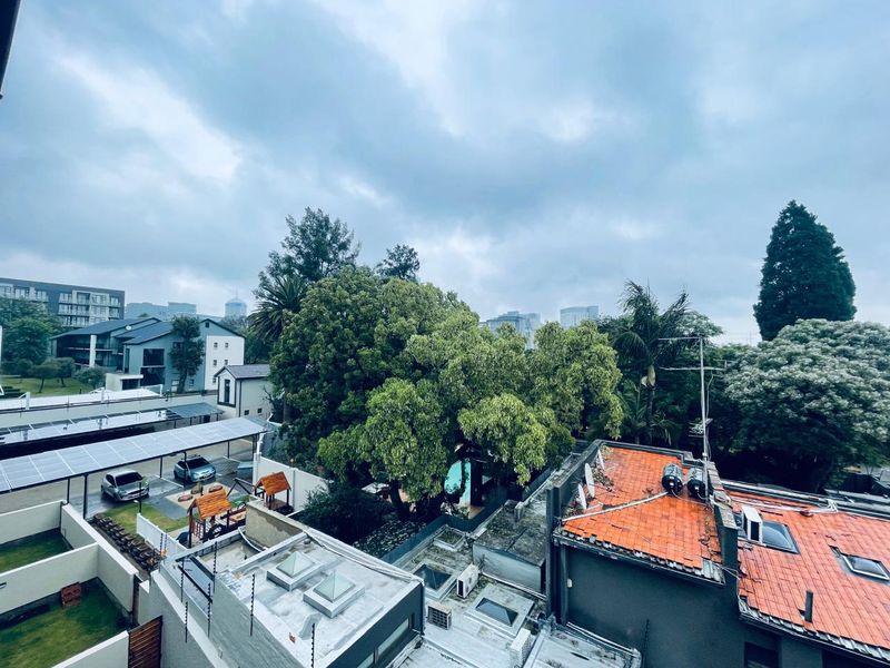 Elevated view overlooking the surrounding residential complex, featuring rooftops with solar panels, skylights, and mature trees under a cloudy sky.