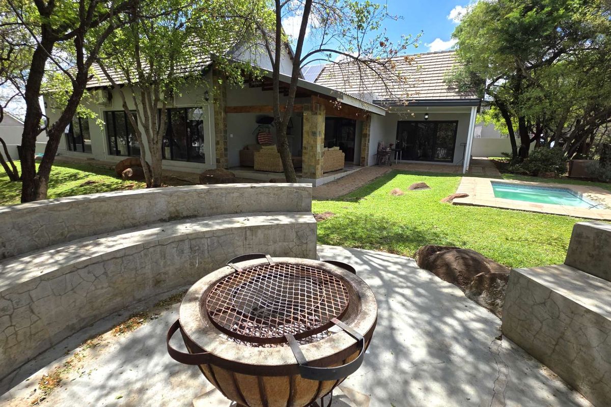 Rear garden featuring a swimming pool, covered patio with stone-clad pillars, and a built-in concrete fire pit area with integrated seating.