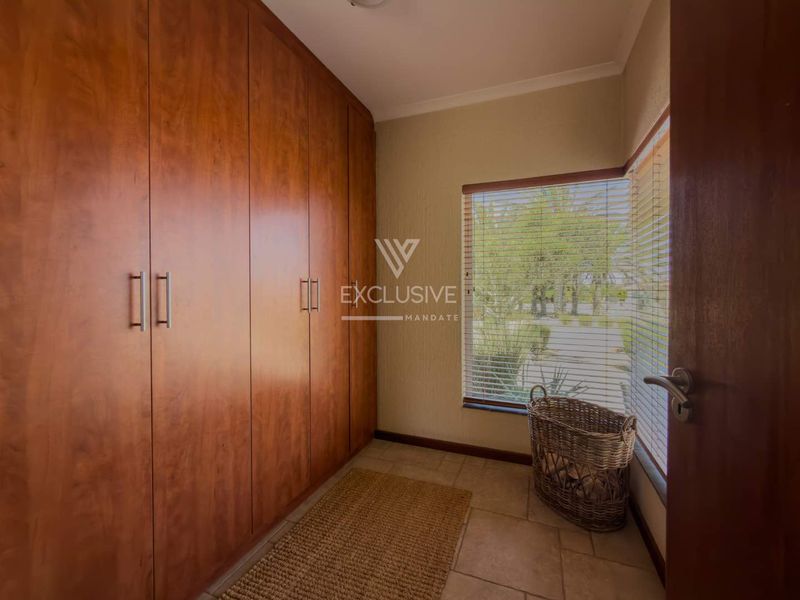 A bedroom featuring extensive floor-to-ceiling built-in wooden cupboards, tiled flooring, and natural light through a window with fitted venetian blinds.