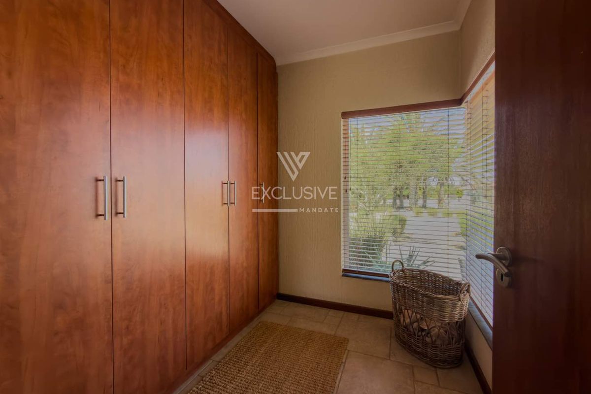 A bedroom featuring extensive floor-to-ceiling built-in wooden cupboards, tiled flooring, and natural light through a window with fitted venetian blinds.