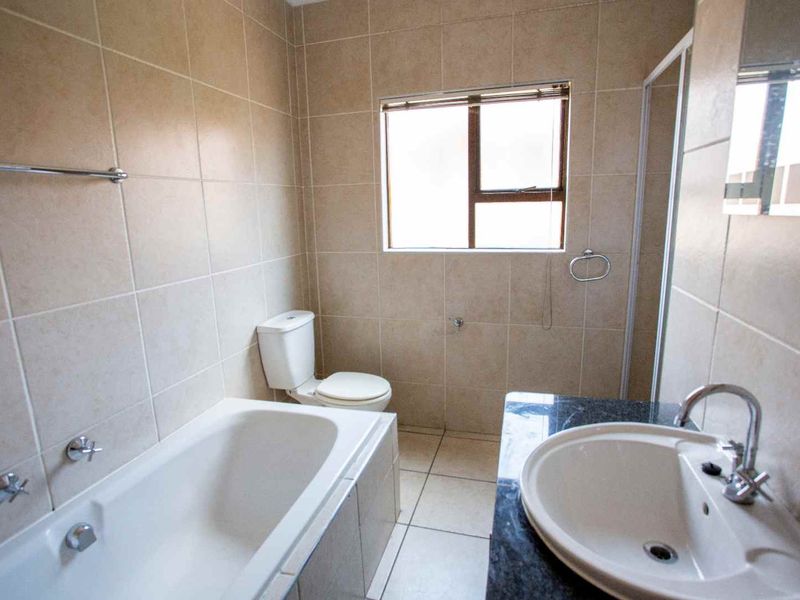 A functional bathroom featuring a built-in bathtub, a separate shower enclosure, a vanity basin with a granite countertop, and neutral wall tiling.