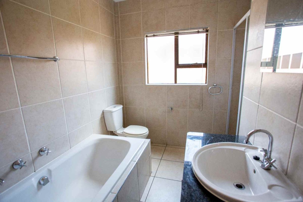 A functional bathroom featuring a built-in bathtub, a separate shower enclosure, a vanity basin with a granite countertop, and neutral wall tiling.