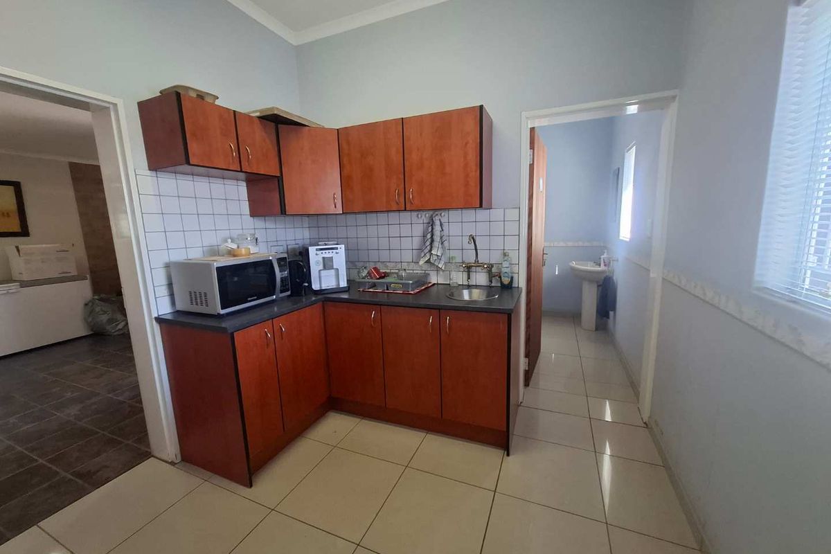 A functional kitchen area featuring wood-look laminate cabinetry, a tiled backsplash, and ceramic floor tiles, providing a practical workspace for office staff.