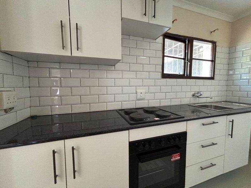 A clean, functional kitchen featuring white cabinetry, dark granite countertops, a subway tile backsplash, and built-in oven and hob.