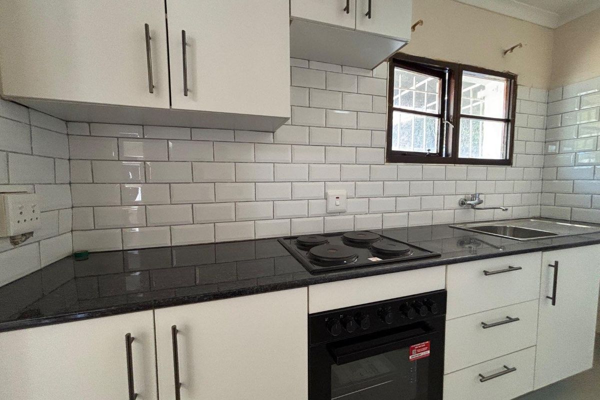 A clean, functional kitchen featuring white cabinetry, dark granite countertops, a subway tile backsplash, and built-in oven and hob.