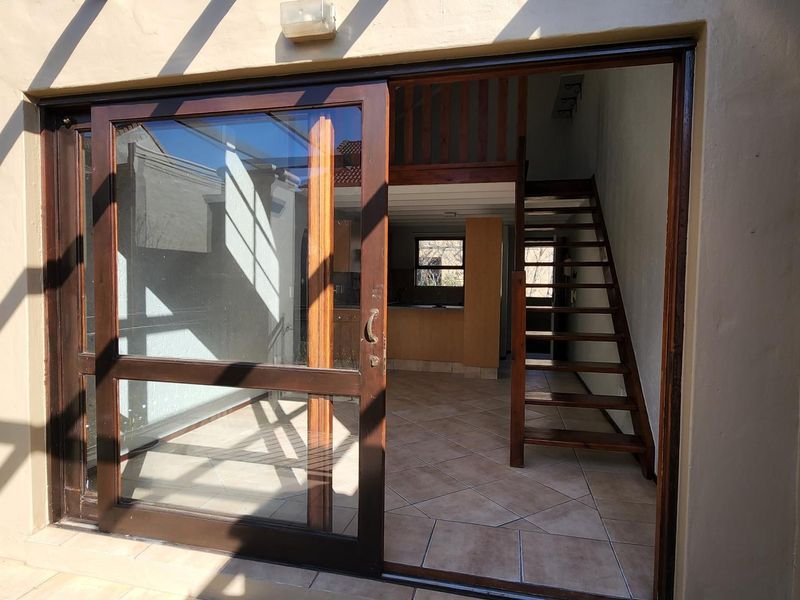 Open plan living area featuring tiled floors, a wooden staircase leading to a mezzanine level, and large sliding glass doors opening to the exterior.