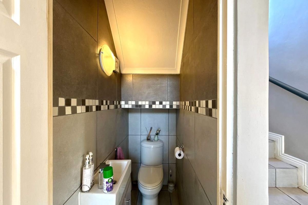 A compact guest bathroom featuring modern tiled walls, a wall-mounted basin, and a standard toilet, situated conveniently near the staircase.