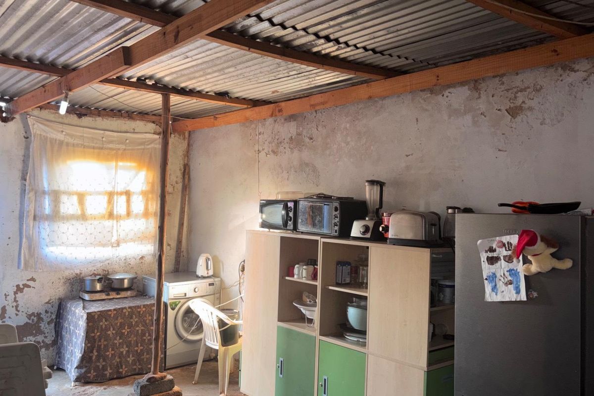 A rustic kitchen area featuring exposed timber rafters, corrugated metal roofing, and unfinished masonry walls, providing a basic utility space.