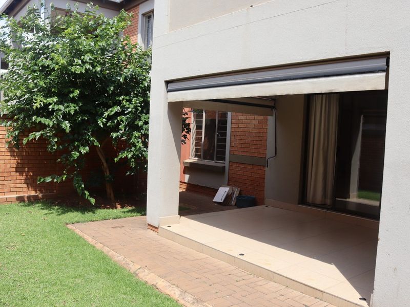 A covered patio area featuring tiled flooring and a retractable awning, providing direct access to the garden through sliding glass doors.