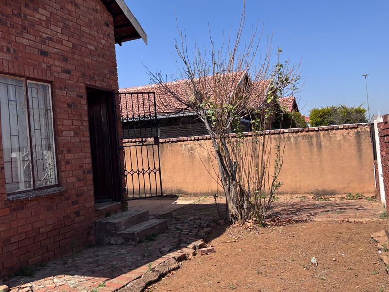 Rear exterior view of a face brick house featuring a paved walkway, security gate, and perimeter wall.