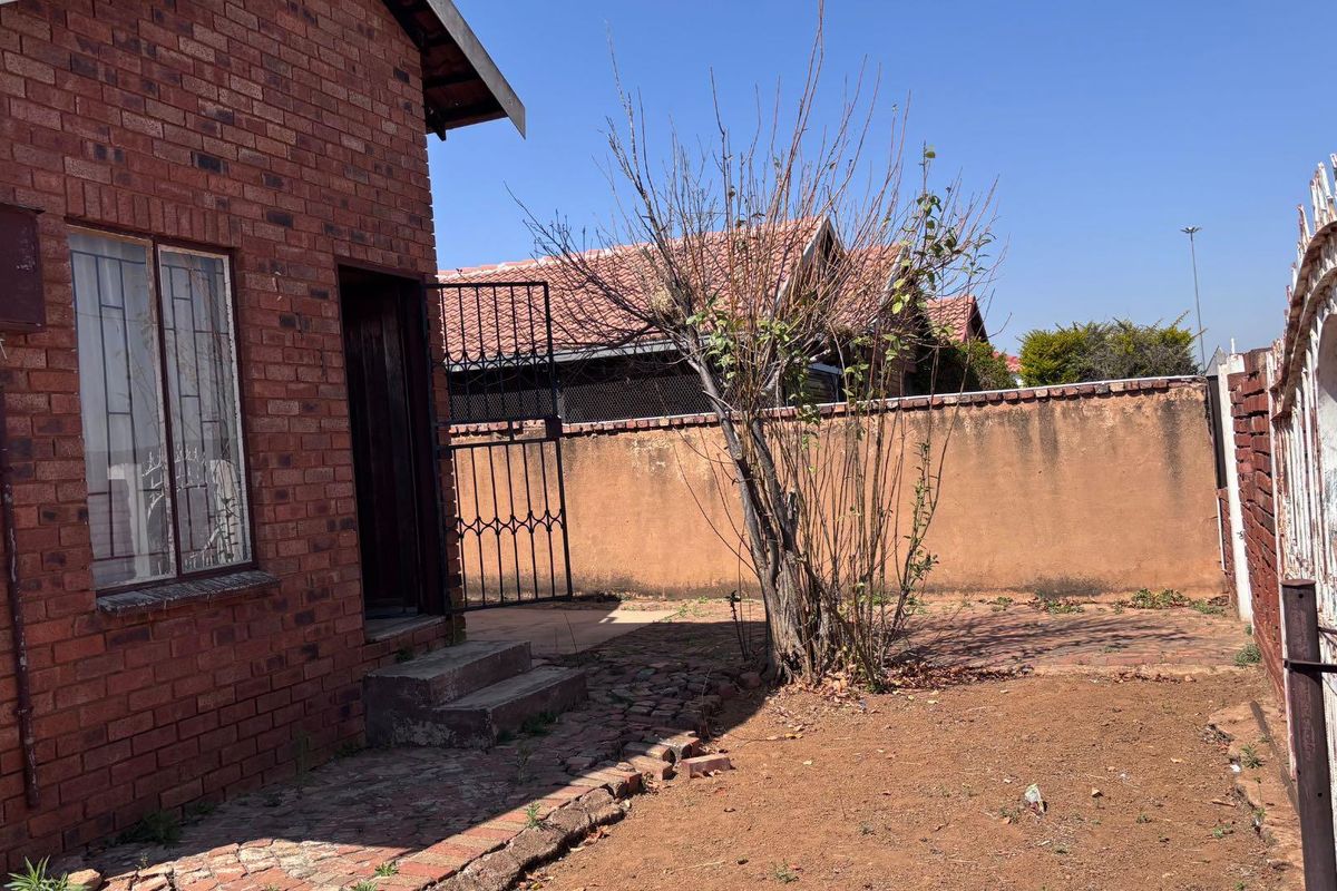 Rear exterior view of a face brick house featuring a paved walkway, security gate, and perimeter wall.